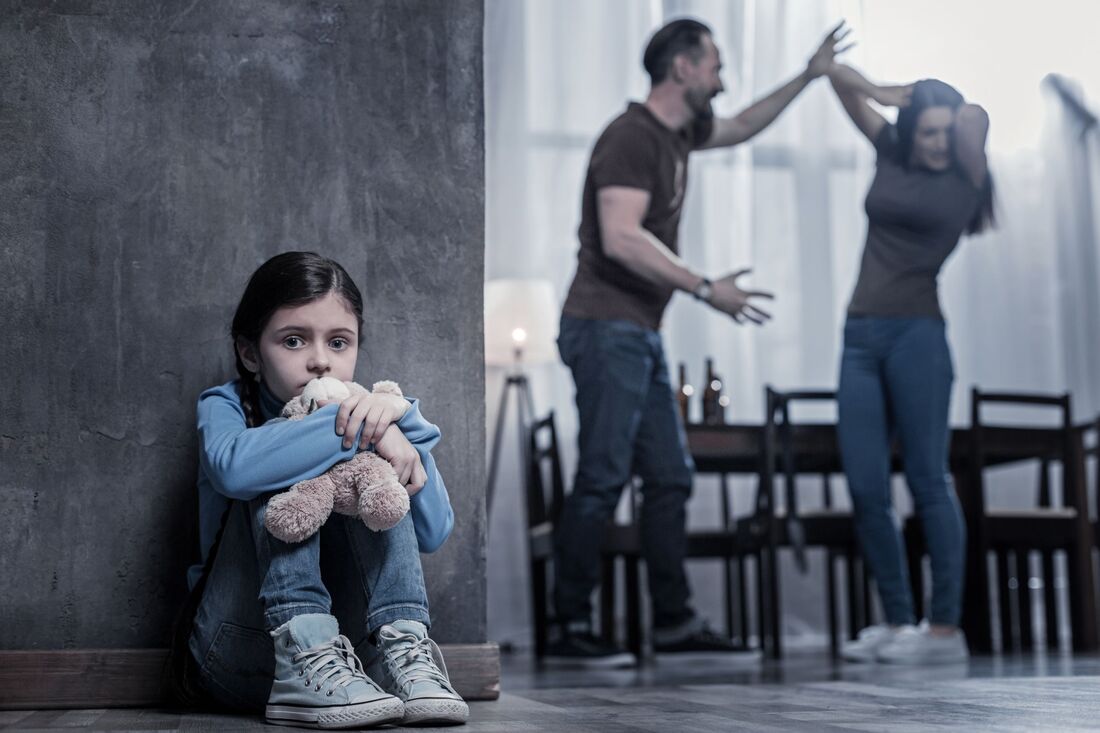 Bildet er er illustrasjonsbilde for dagdaer om vold. Bildet viser et barn som sitter på gulvet med foreldre som krangler og er fysiske i bakgrunnen. Foto: Shutterstock